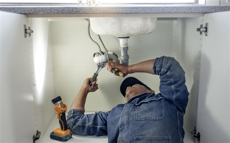 Plumber repairing pipes beneath a bathroom sink in Miami Beach