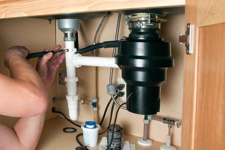 Plumber installing a garbage disposal beneath a kitchen sink in Miami Beach