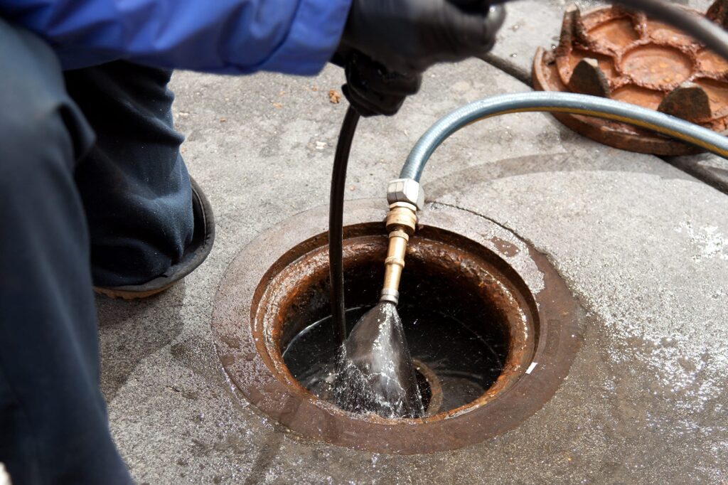 Plumber hydro jetting a sewer line through a manhole in Miami Beach