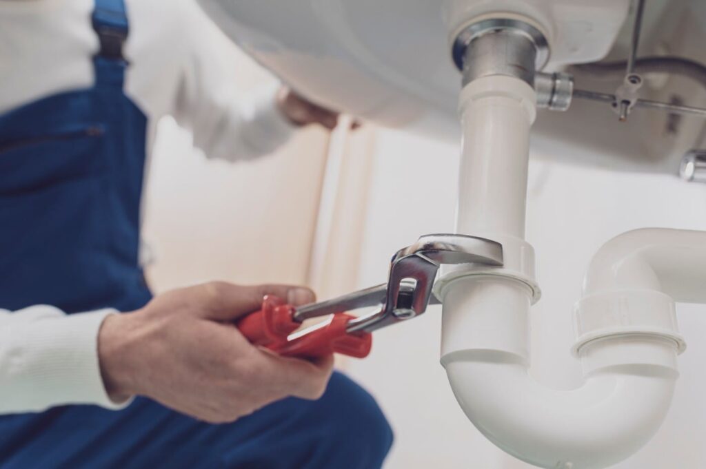 Plumber repairing a white drain pipe beneath a sink in Miami Beach