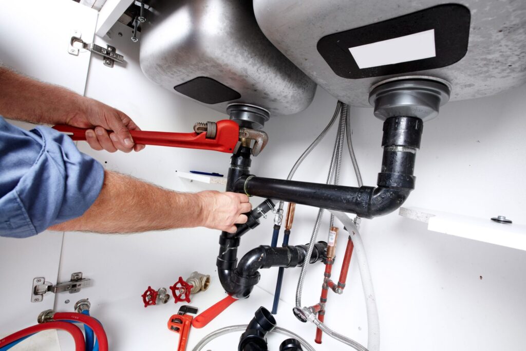 Plumber repairing drain pipes beneath a kitchen sink in Miami Beach